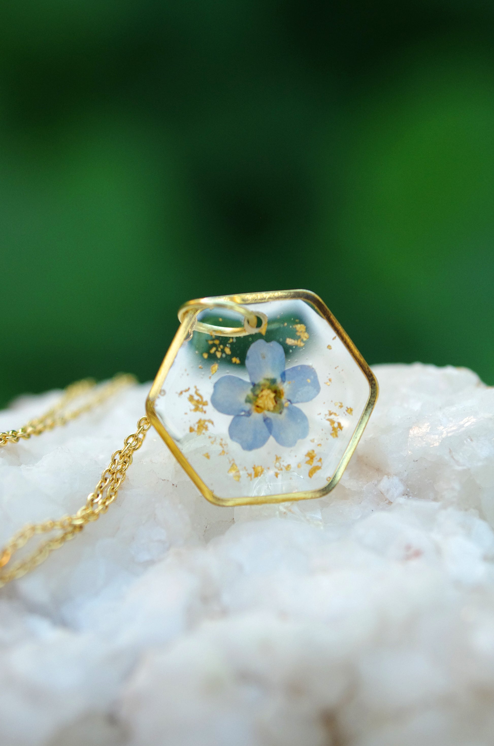 Close up image of a blue forget me not necklace with gold leaf